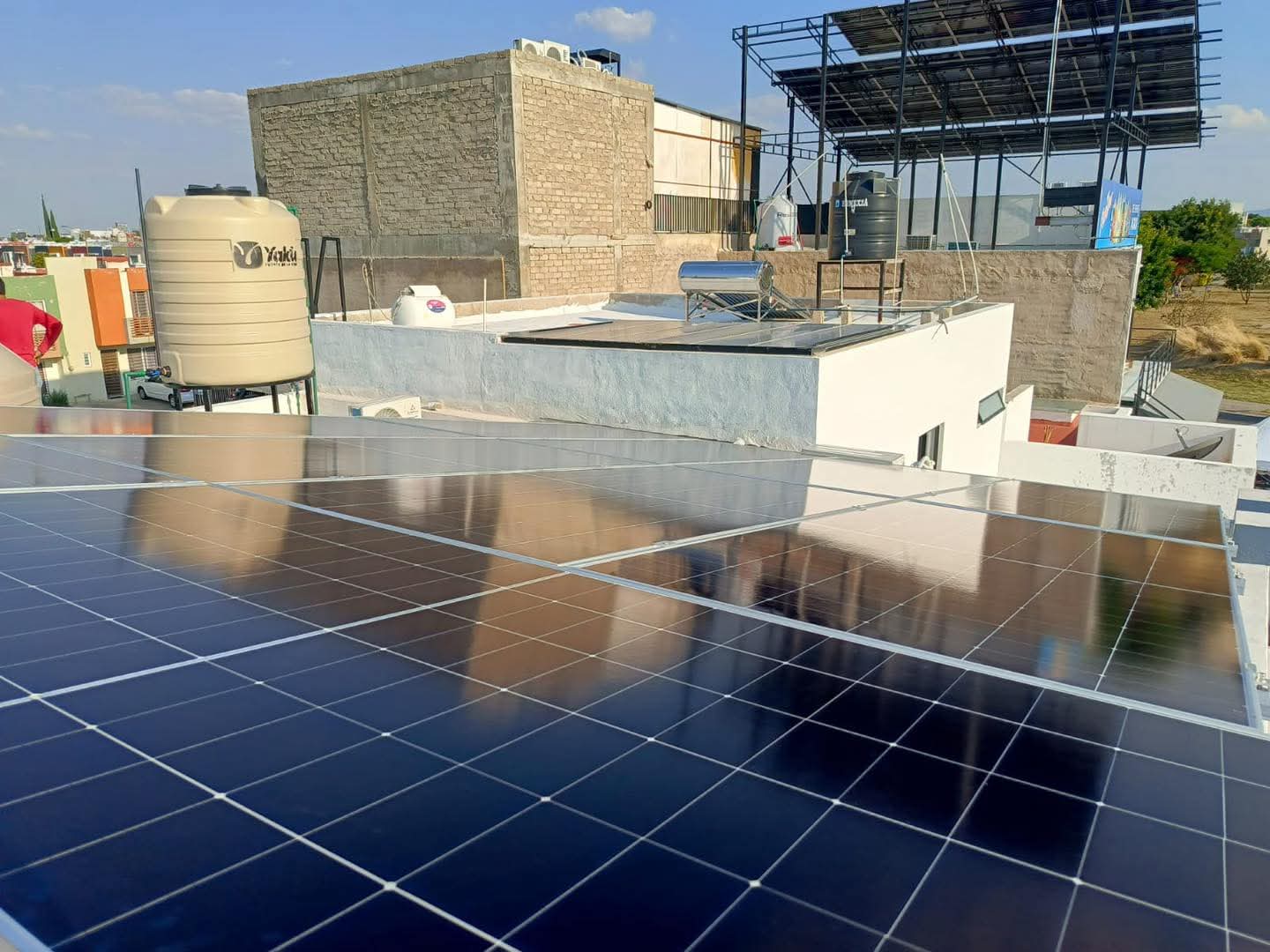 Paneles solares inclinados en una azotea de Campo Real, Zapopan, junto a un tinaco beige